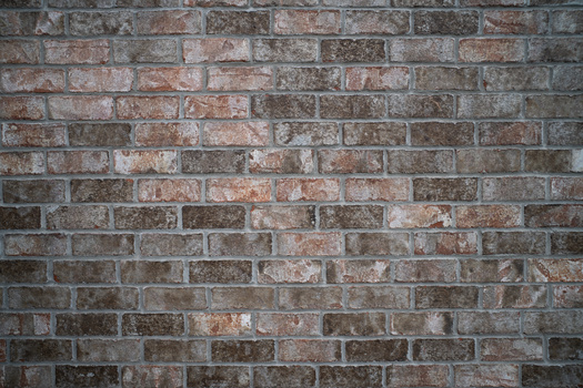 Weathered brick wall with varied red, brown, and gray tones in running bond pattern.