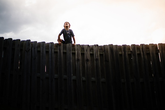 Person standing on top of a tall wooden fence against a cloudy sky.