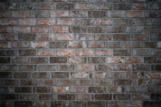 Close-up of weathered brick wall with varied red, brown, and gray tones and visible mortar joints.
