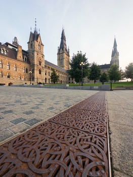 Gothic and Victorian stone buildings with spires overlook a paved plaza with decorative metalwork inlay.