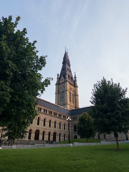 Gothic Revival church with tall spire dominating a green lawn, framed by mature trees under clear sky.