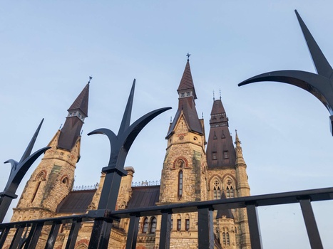Gothic stone church with multiple spires framed by ornamental black metal fence in foreground.