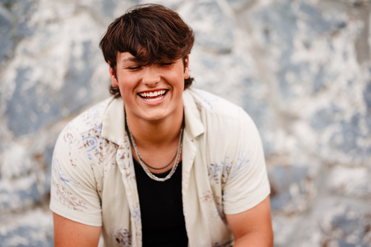 Young man with dark hair smiling at camera against textured white and blue background.