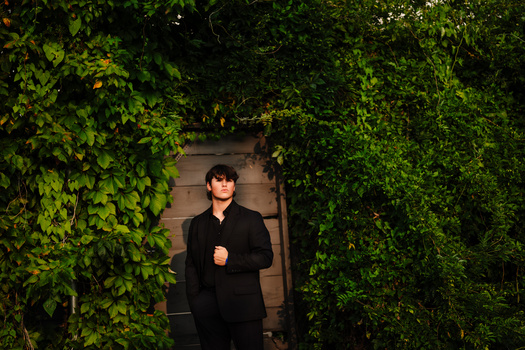 Person in black clothing standing between ivy-covered walls in narrow passage.