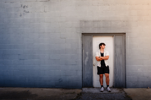 Athletic person standing in doorway of plain concrete building holding a basketball.