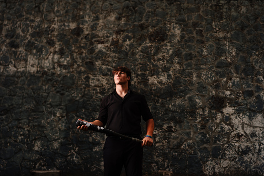 Person in black clothing holding a rifle against a weathered concrete wall.