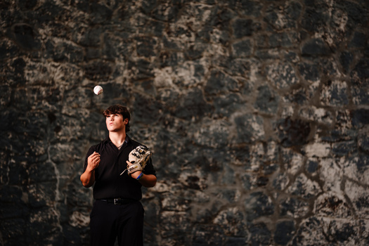 Baseball player in black uniform preparing to catch a ball against a weathered concrete wall.