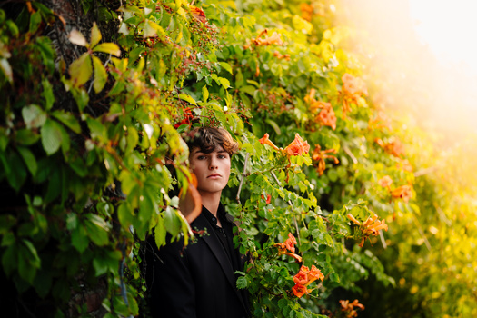 Young man in dark clothing surrounded by green and golden autumn foliage in warm sunlight.