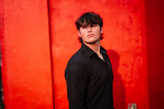 Young man in black shirt against vibrant red backdrop, looking toward camera.