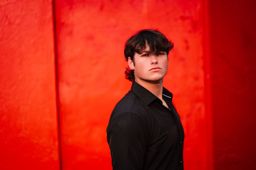 Young man in black shirt against vivid red backdrop, looking away from camera.