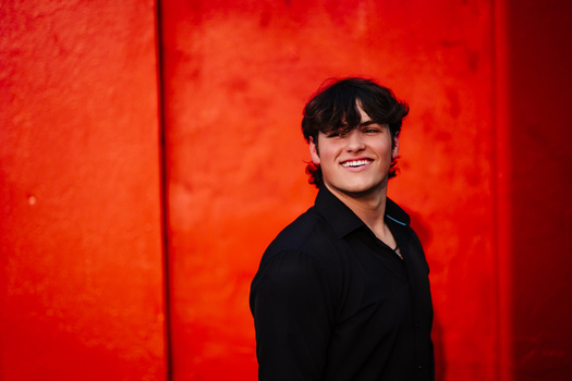 Young man in black shirt smiling against vibrant red background.