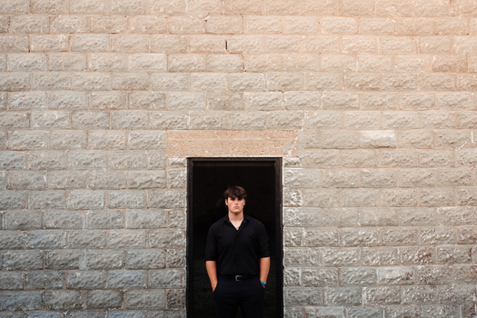 Person in black shirt standing in dark doorway of tan brick wall.