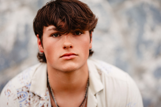Young man with dark hair wearing a light button-up shirt, looking directly at camera with neutral expression.