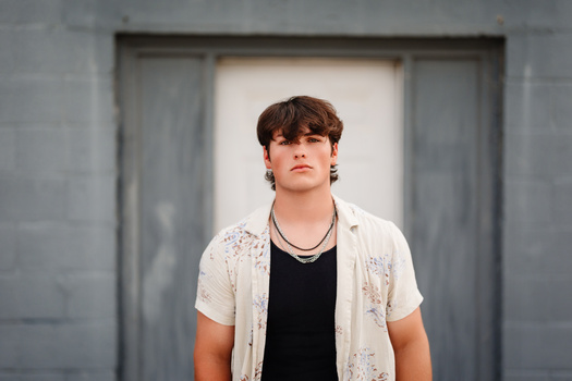 Young man in casual wear standing against a minimalist concrete backdrop with neutral lighting.