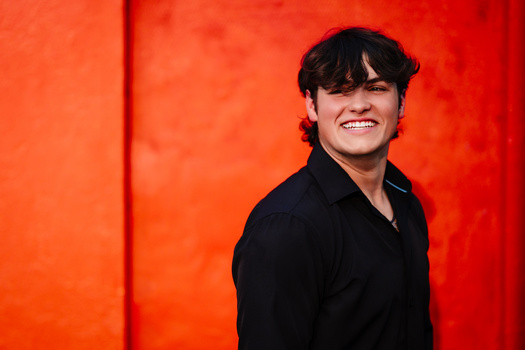 Young man smiling at camera against a vibrant red-orange backdrop.