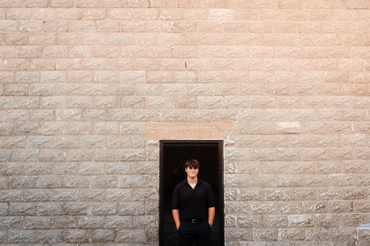 Person in dark clothing framed by a dark rectangular opening in a light brick wall.
