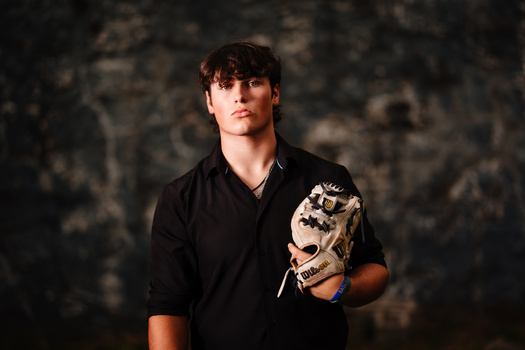 Young man in black shirt holding a decorative skull mask against a textured dark background.