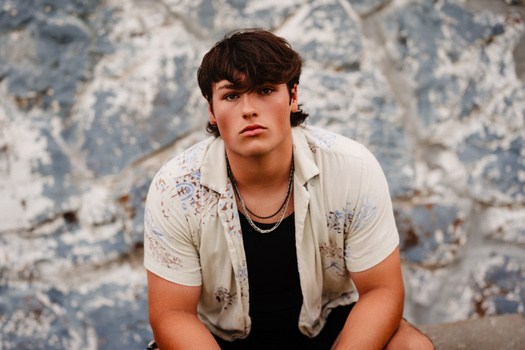 Young man in casual button-up shirt against weathered textured wall.
