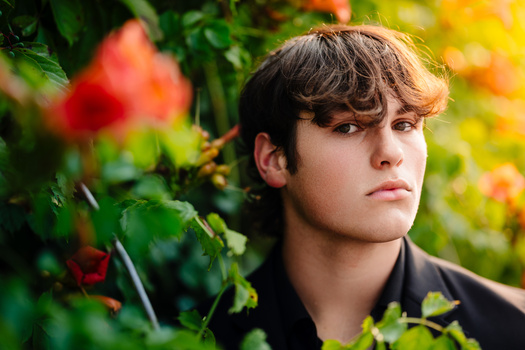 Young person with tousled brown hair gazing thoughtfully among blooming red and yellow flowers.