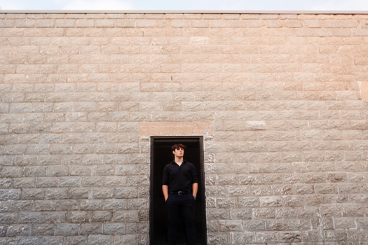 Person in black clothing standing in doorway of tan brick wall.
