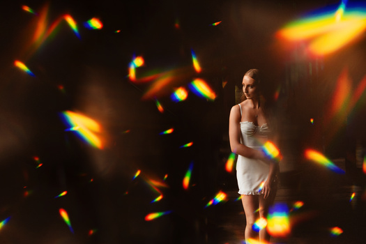 Woman in white dress standing amid colorful light streaks and bokeh effects against dark background.
