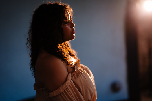 Woman in profile backlit by warm golden sunlight against a cool blue background.