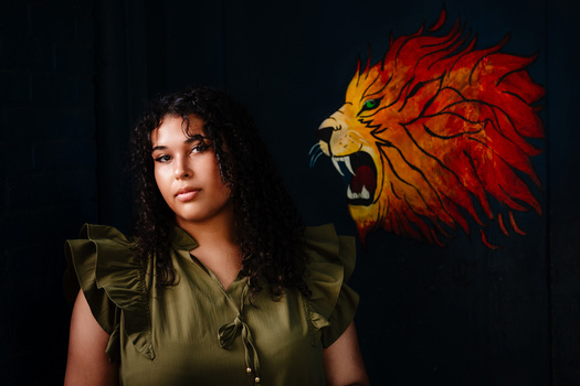 Woman in olive green top with dark curly hair gazing toward a roaring lion illustration on black background.