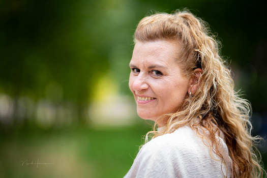 Woman with wavy blonde hair smiling over her shoulder in outdoor portrait.