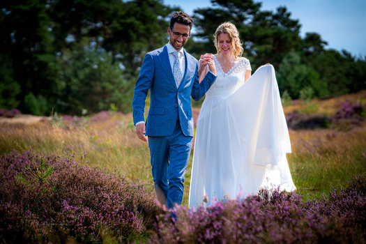 Bride and groom walking through a blooming heather field on their wedding day.