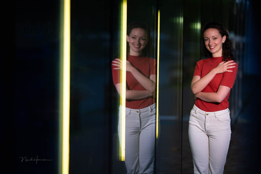 Two women in red shirts and white pants posing between glowing vertical neon light tubes.