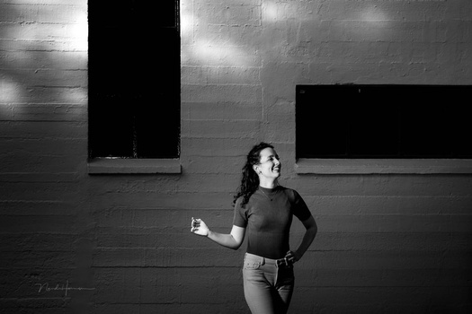 Woman in dark shirt running against textured concrete wall with dark window openings.