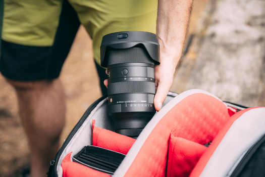 Photographer holding a camera with telephoto lens mounted on a red camera bag.