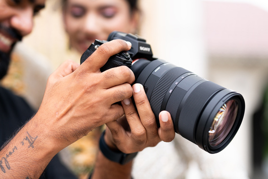 Photographer's hands holding a DSLR camera with a telephoto lens attached.