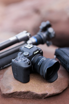 Professional camera with attached lens on sandy surface, surrounded by photography equipment and cables.