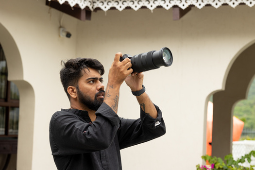 Photographer holding a telephoto lens up to his eye while composing a shot outdoors.