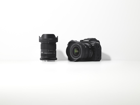Black mirrorless camera body with detached wide-angle lens featuring lens hood on white surface.