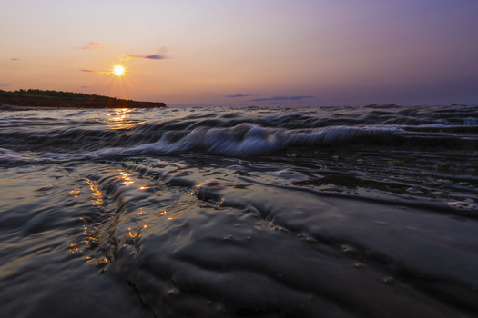 Ocean waves at sunset with golden light reflecting off the water and darkening sky.