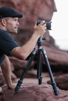 Photographer using a camera mounted on a tripod to compose a shot in a desert landscape.