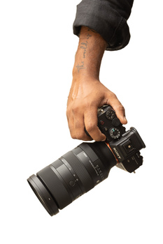 Photographer's hand holding a digital camera with telephoto lens against white background.
