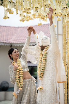 Woman in traditional dress arranging hanging golden flower garlands against white fabric backdrop.