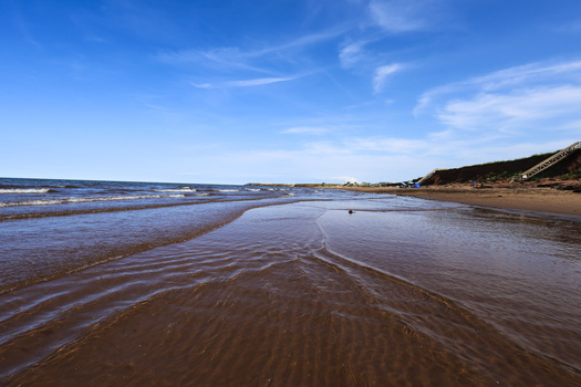 Expansive beach at low tide with rippled wet sand and shallow pools reflecting blue sky.