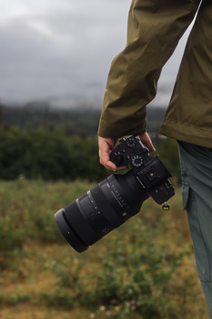 Photographer holding a telephoto lens with a misty forested landscape in the background.