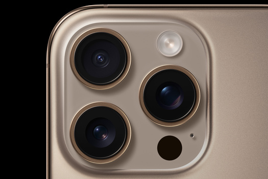 Close-up of a smartphone's rear camera system with three large lenses and a flash module on a metallic beige body.
