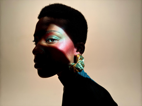 Profile portrait with dramatic colored lighting and bold makeup against neutral background.