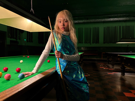 Woman in blue sequined vest holding pool cue at billiards table with colored balls.