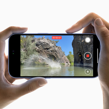 Smartphone held in both hands displaying a landscape scene with rocky cliffs and water during video recording.