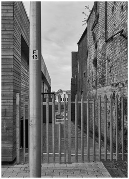Metal gate opening onto a narrow urban alley between brick buildings under overcast sky.