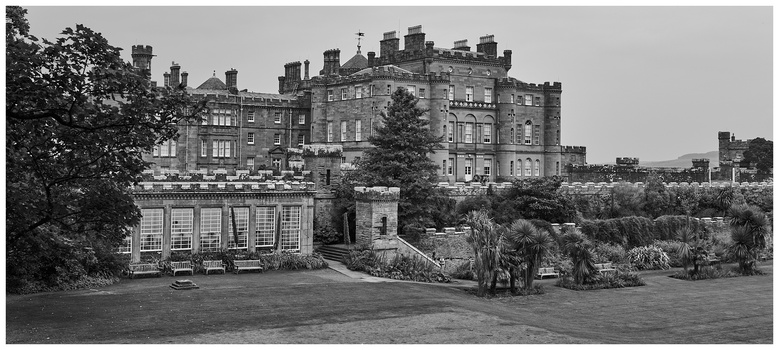 Black and white photograph of a grand stone castle with manicured grounds and formal gardens in the foreground.