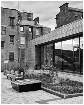 Modern glass-fronted extension adjoining historic brick buildings around a paved courtyard with planters.