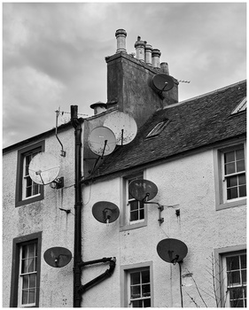 Black and white photograph of a whitewashed residential building with multiple satellite dishes mounted on its roof and exterior walls.